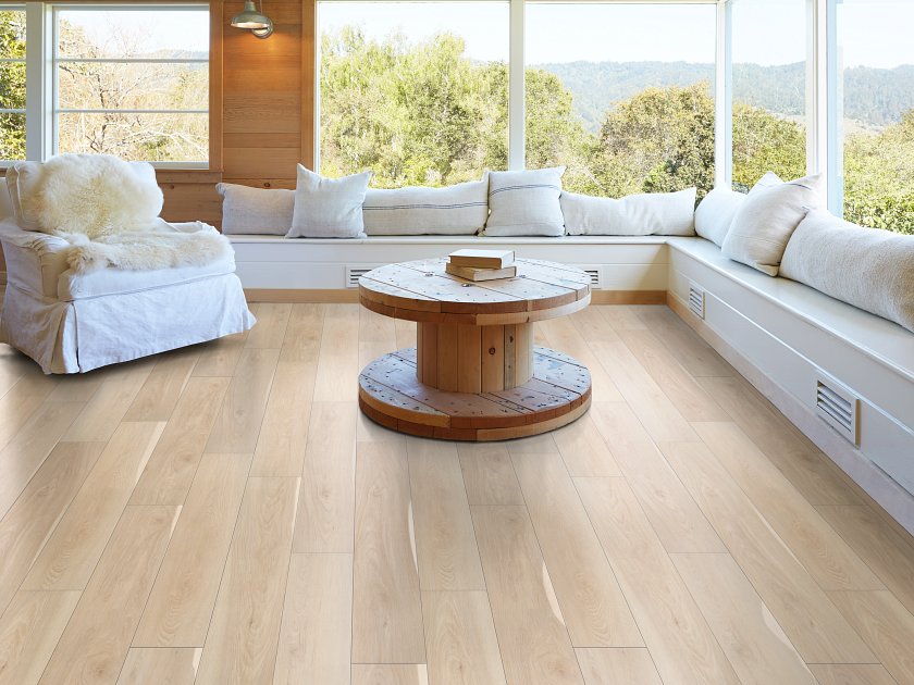 Light-toned waterproof luxury vinyl plank flooring in a sunlit living room with built-in seating and large windows